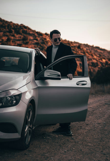 stoere man staat met een zonnebril naast zijn auto met de deur open