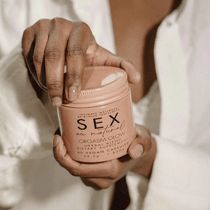 Handen in witte blouse houden een perzikkleurige pot met het label ‘SEX’ vast, luxe intiem verzorgingsproduct