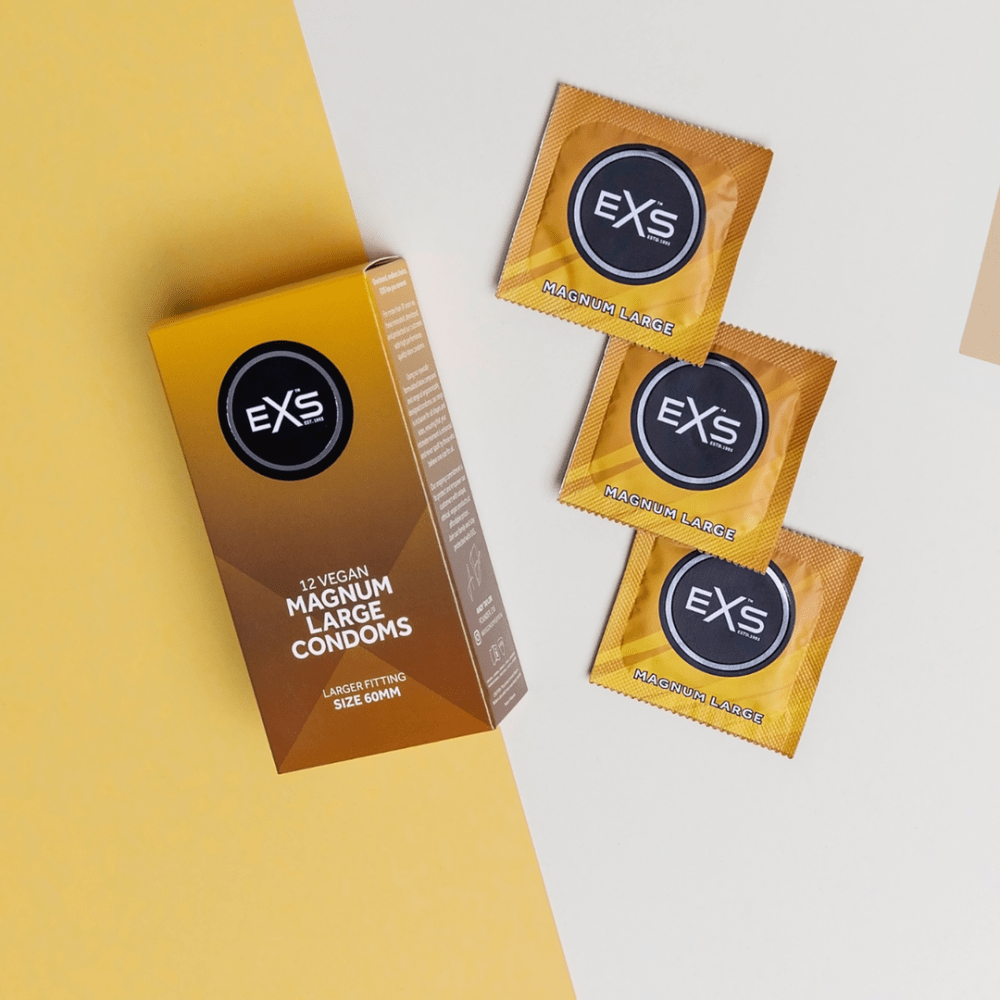 EXS Magnum condooms met doosje en meerdere goudbruine sachets, speels neergelegd op witte en gele vlakken.