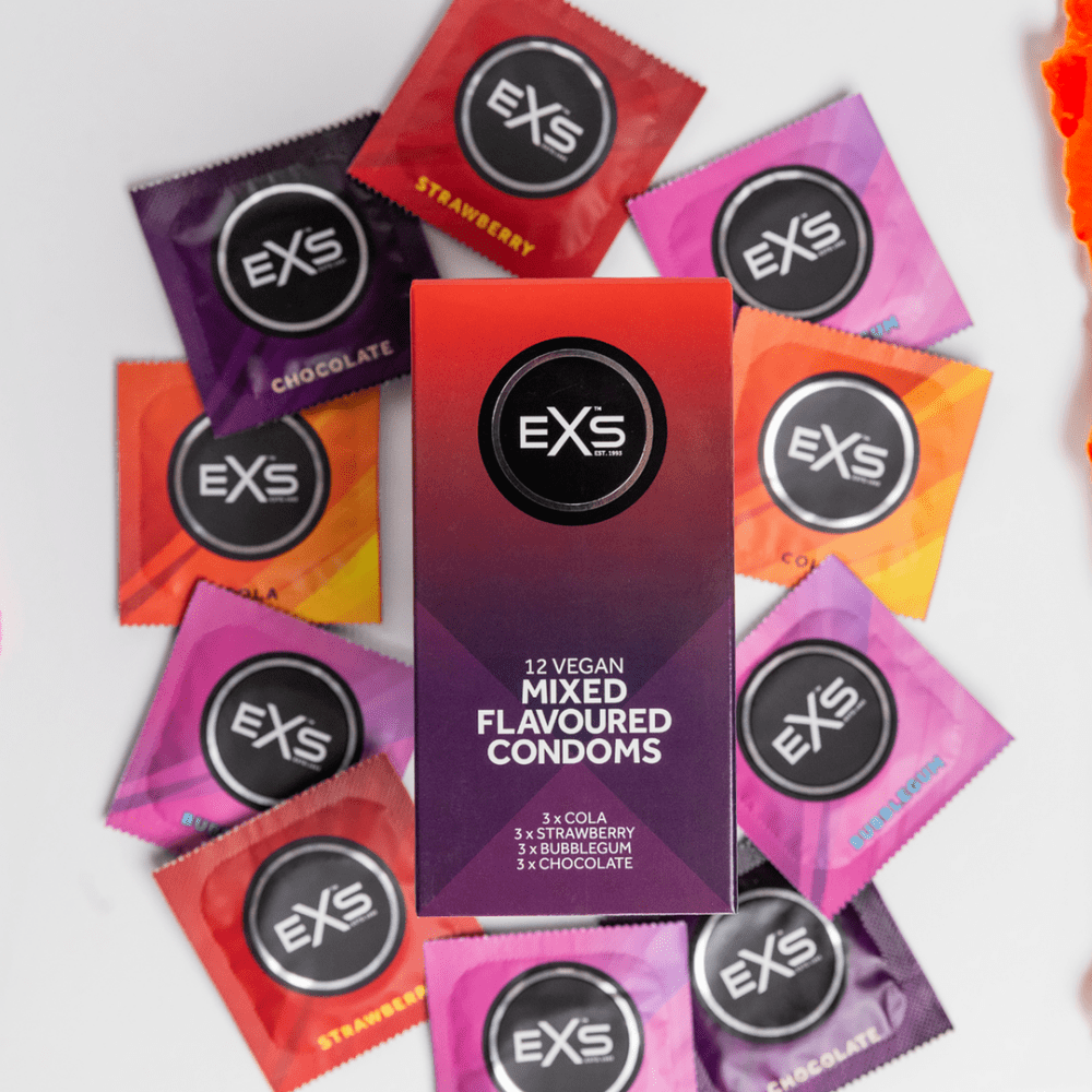 Losse EXS Mixed Flavoured condooms in smaakvarianten, speels verspreid op een roze achtergrond