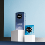 EXS Snug Fit condooms als sfeerbeeld met doosje en losse wrapper op witte sokkels tegen blauwe achtergrond