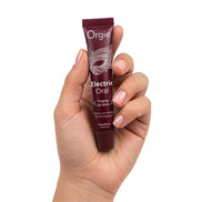 Hand houdt Orgie Electric Oral tintelende lipgloss aardbei vast, met bordeauxrode tube zichtbaar