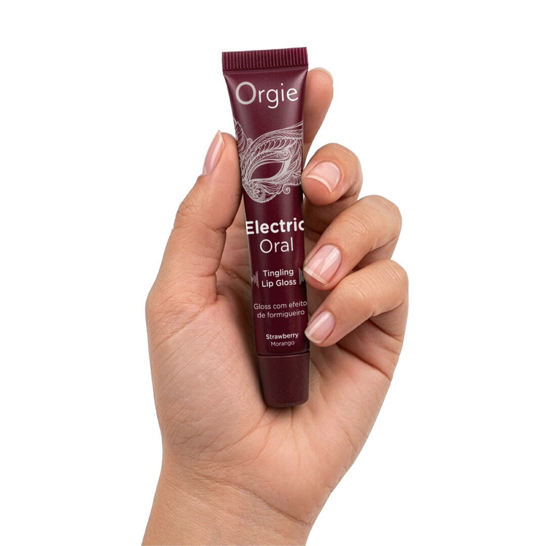 Hand houdt Orgie Electric Oral tintelende lipgloss aardbei vast, met bordeauxrode tube zichtbaar
