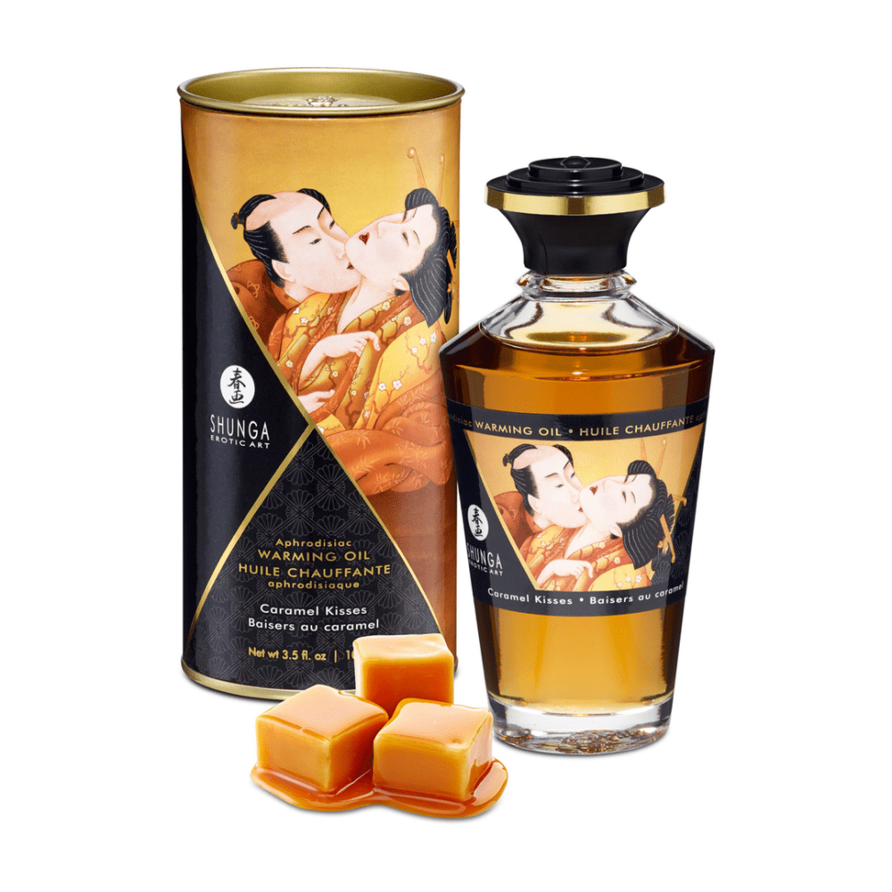 Shunga Aphrodisia Olie Caramel Kisses 100 ml met verpakking, fles en karamelstukjes ernaast