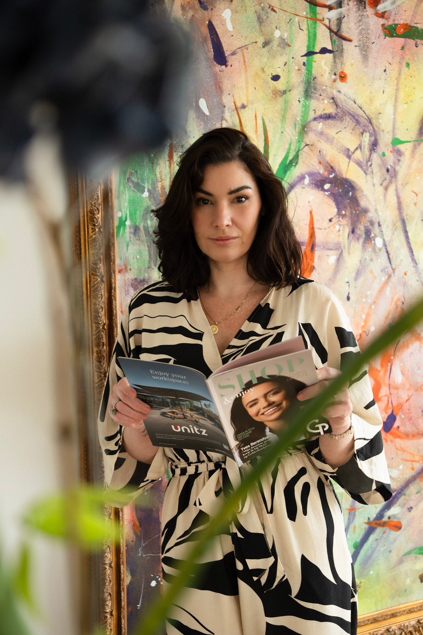 Vrouw in zwart-witte kimono leest tijdschriften bij kleurrijk kunstwerk, met plantbladeren op de voorgrond