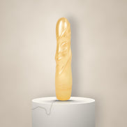 Glanzende gouden vibrator met gestileerd bladreliëf, rechtop op een witte marmeren sokkel tegen een zachte crèmekleurige achtergrond