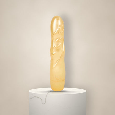 Glanzende gouden vibrator met gestileerd bladreliëf, rechtop op een witte marmeren sokkel tegen een zachte crèmekleurige achtergrond