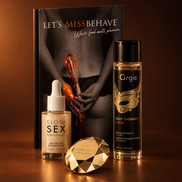 Het boek Let's MissBehave, Where food meets pleasure, naast Slow Sex Shimmer Dry Oil, Orgie Sexy Therapy Amor massageolie en een goudkleurig diamantvormig accessoire, warm uitgelicht op een koperbruine achtergrond