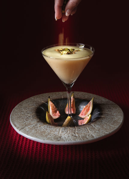 Romig dessert in cocktailglas met vijgen op een bord, terwijl een hand fijne topping toevoegt