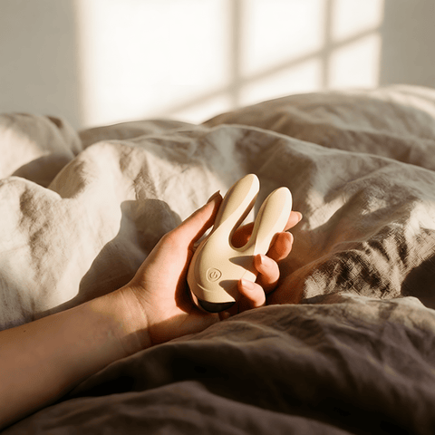 Beige Odes Sense wand vibrator in een hand op een zacht bed, gefotografeerd in warm natuurlijk licht