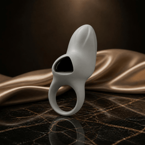 Lichtgrijze Odes Surrender vibrerende ring met zwart detail op zwart marmer met goudkleurig satijn