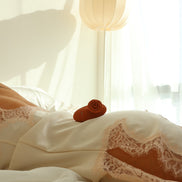 The Touch clitorisvibrator op ivoorkleurige lingerie met kant, sfeervol gefotografeerd in warm daglicht