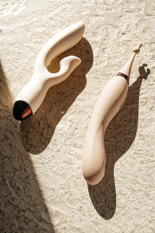Odes vibrators in zachte crèmekleur op een ruwe beige ondergrond met warm licht en luxe schaduwspel
