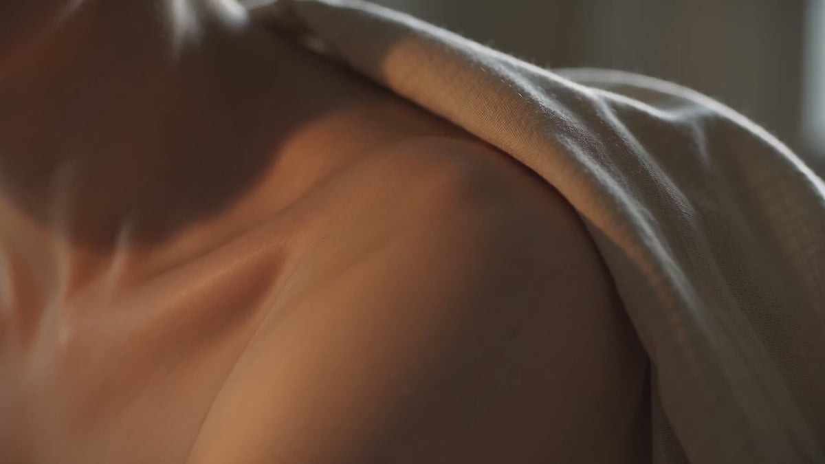 Close-up van een blote schouder en sleutelbeen in warm licht, half bedekt door zachte crèmekleurige stof