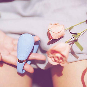 Lichtblauwe vibrator in de hand naast roze rozen, zacht en luxe sfeerbeeld voor Touch-Me nieuwsbrief