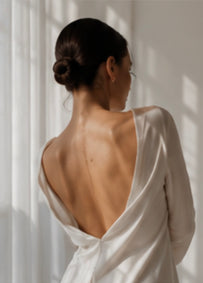 Vrouw in witte jurk met open rug bij zacht raamlicht, elegant sfeerbeeld voor de Touch-Me nieuwsbrief