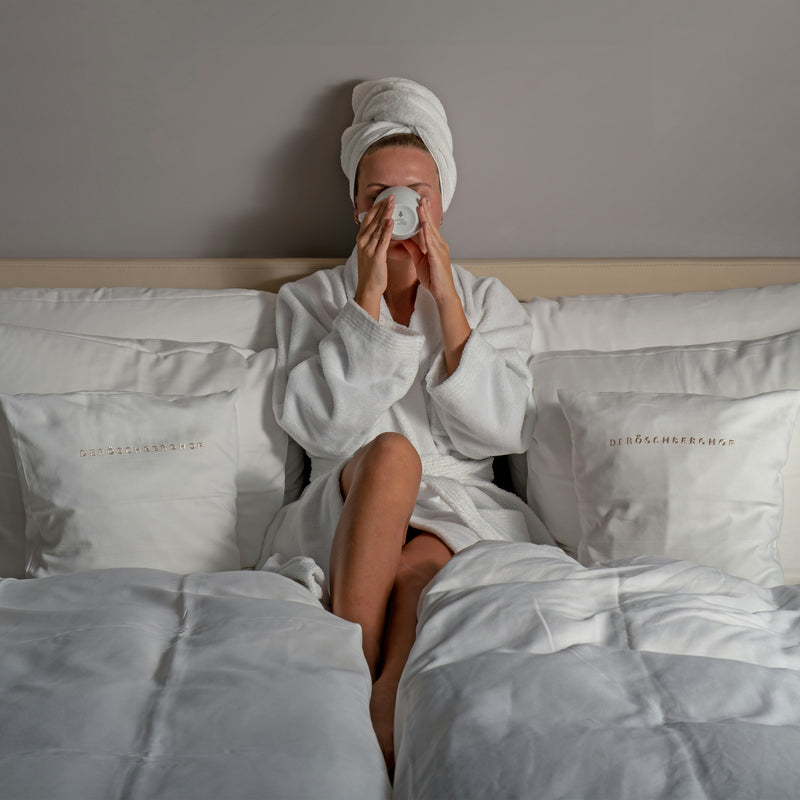 vrouw op bed met koffie en handdoek om haar haar