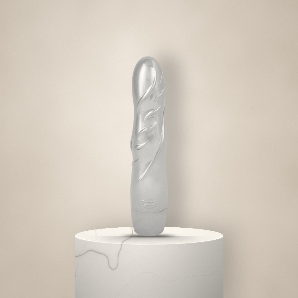 Glanzende zilveren vibrator met gestileerd bladreliëf, rechtop op een witte marmeren sokkel tegen een zachte crèmekleurige achtergrond