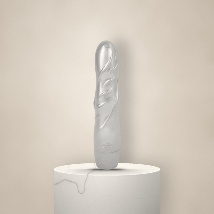 Glanzende zilveren vibrator met gestileerd bladreliëf, rechtop op een witte marmeren sokkel tegen een zachte crèmekleurige achtergrond